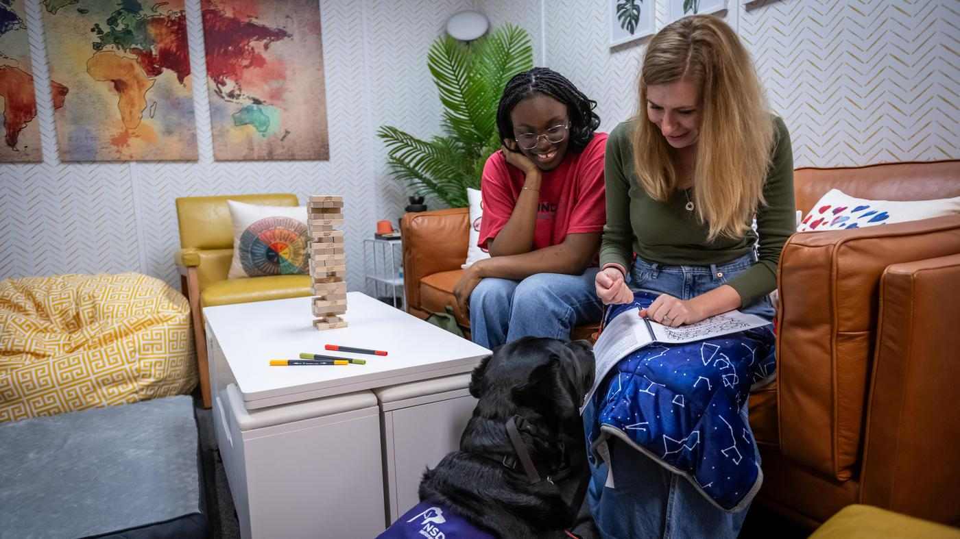 two students sit together in the Kind Space at Fanshawe, working with Heartley, the facility's dog for Canine Assistance Intervention