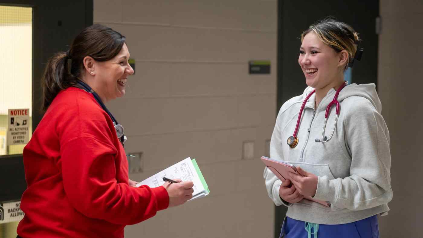 two nursing students with stethoscopes and clipboards laugh together