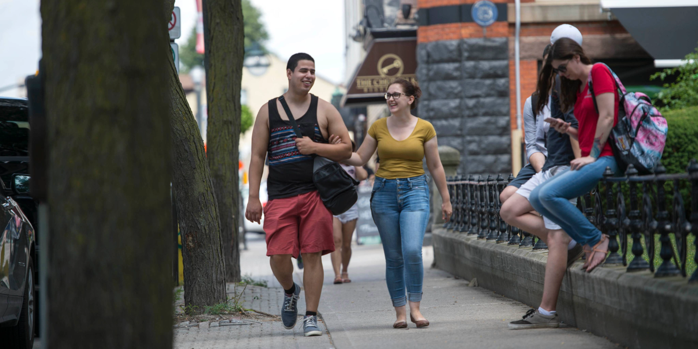 Students walking down a downtown street in the summer heat.