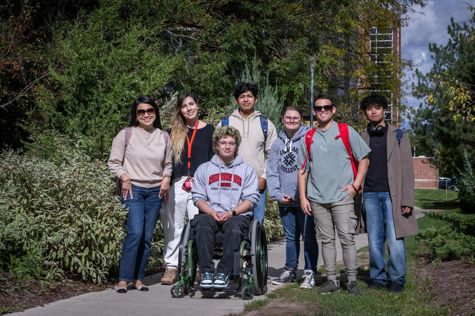 A group poses on a pathway at Fanshawe College's London Campus, with lush greenery and a brick building in the background.