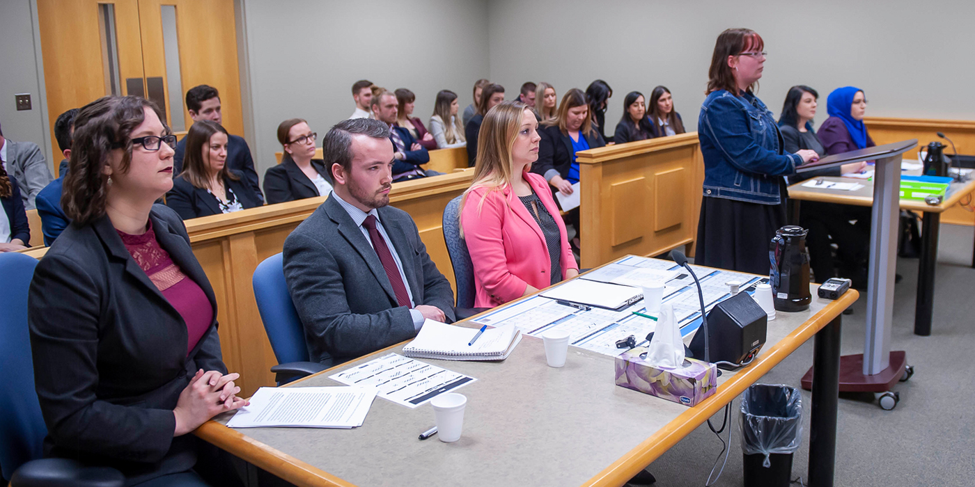 Students in formal attire sit in rows in a courtroom