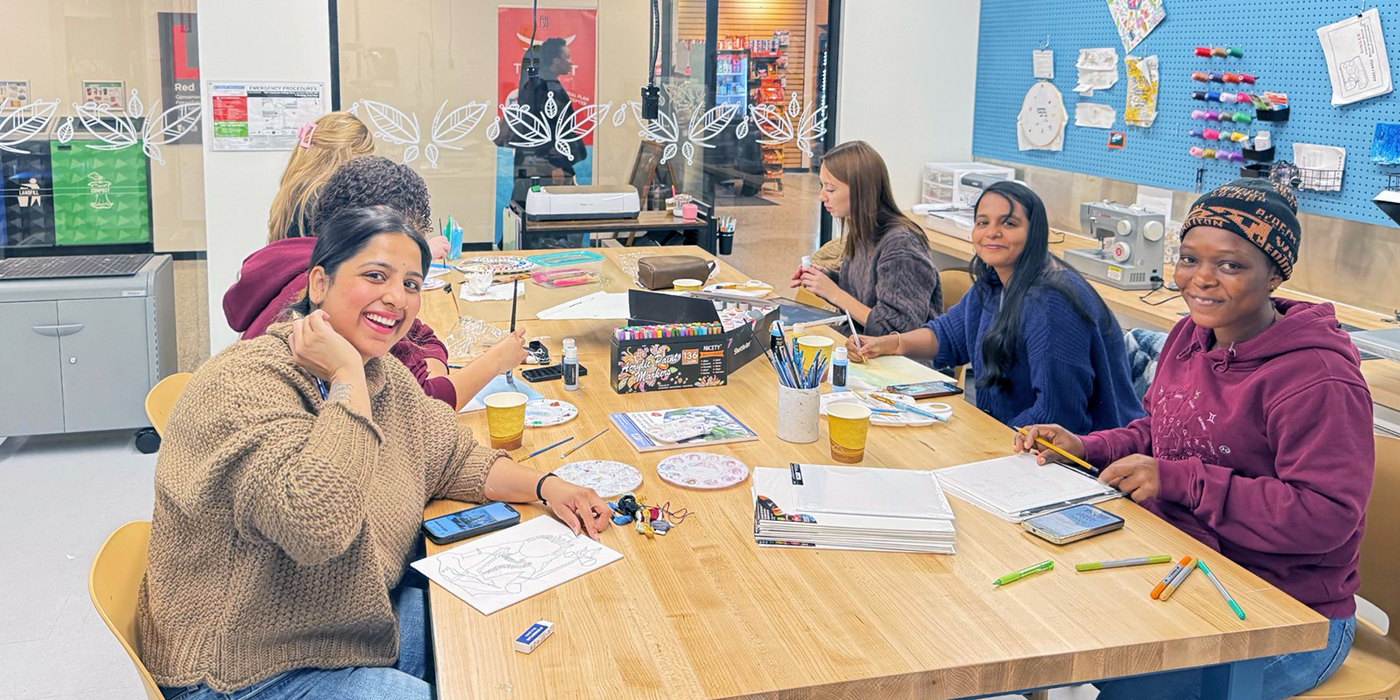 Five students at a table, smiling and working on creative projects