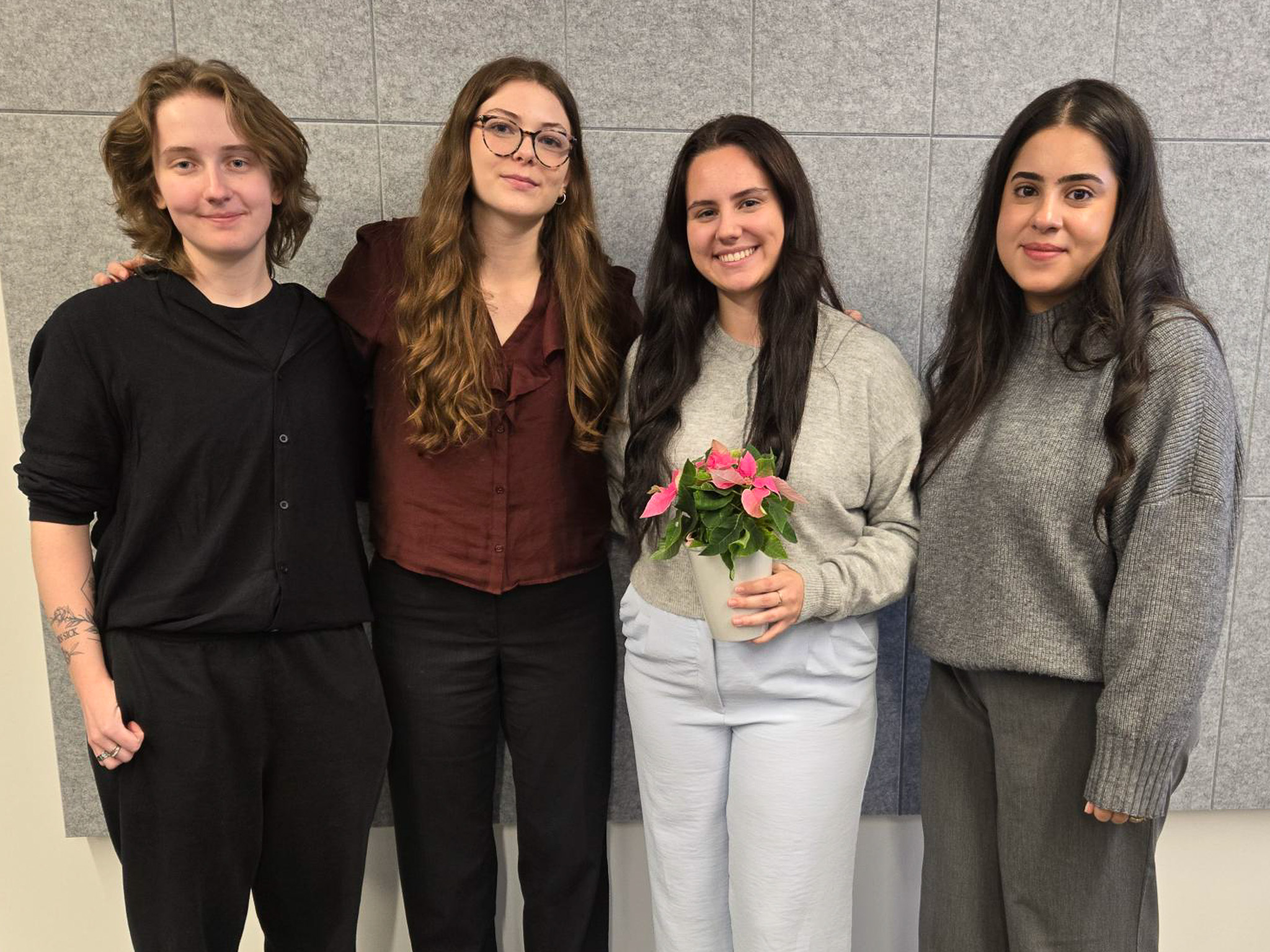 Four students stand in a line smiling at the camera. One student holds a flower pot.