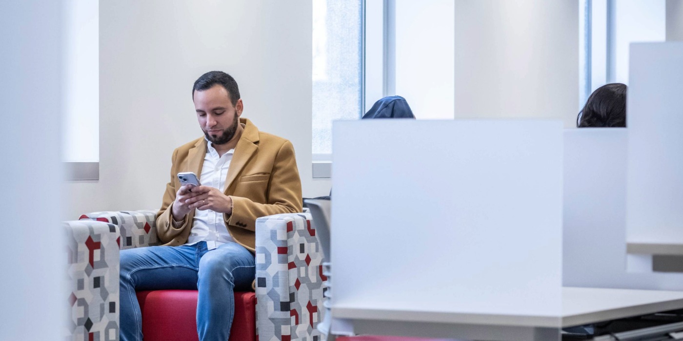 Student sits in a study room completing something on his phone.