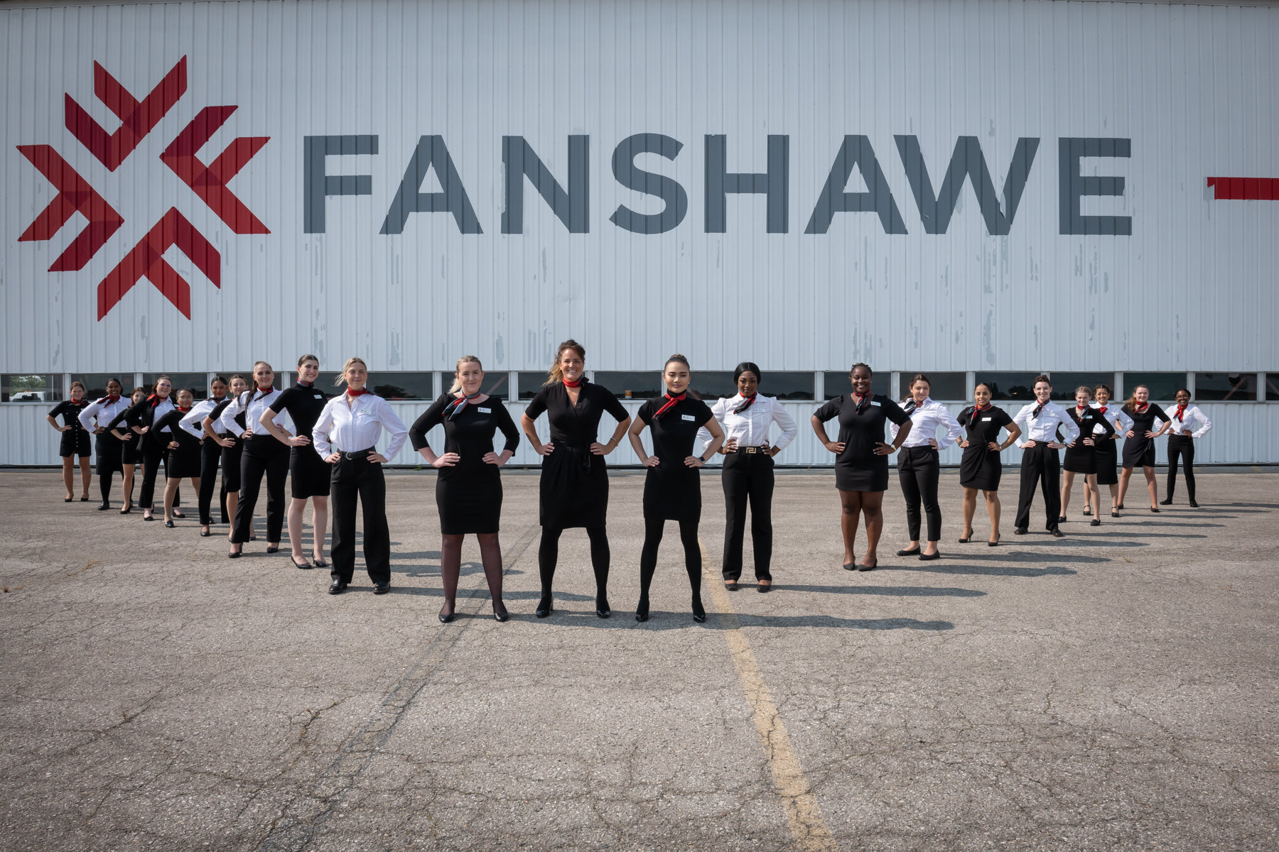 Faculty and students from the Flight Services program line up in uniform in front of the large sliding doors to the hangar which is decorated in a huge Fanshawe logo