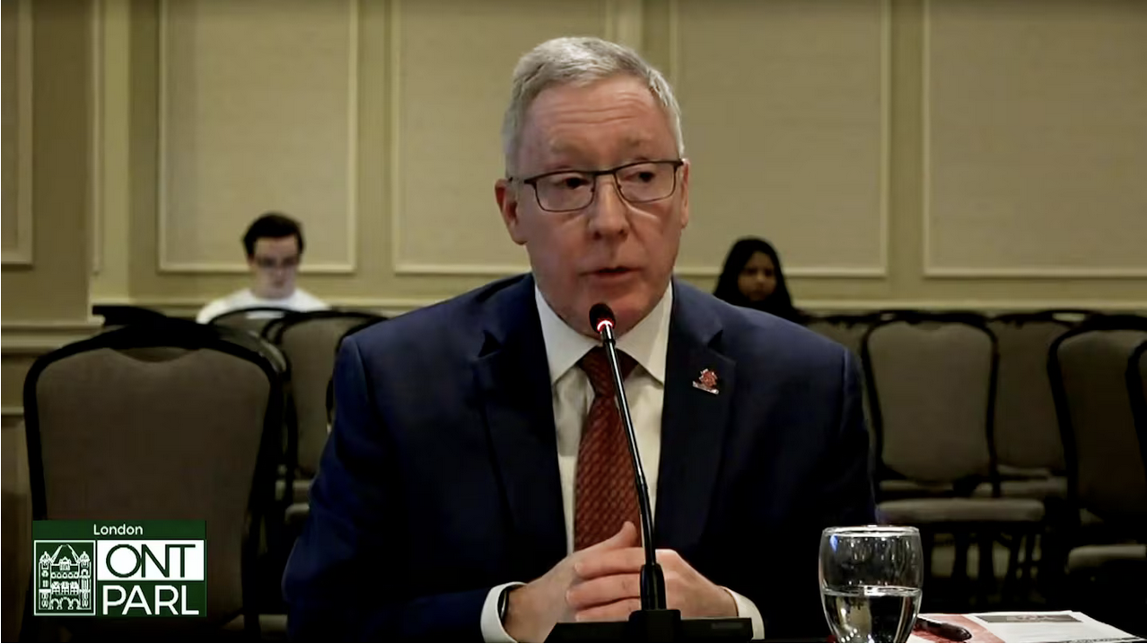 President Peter Devlin is seated at a table speaking into a microphone.
