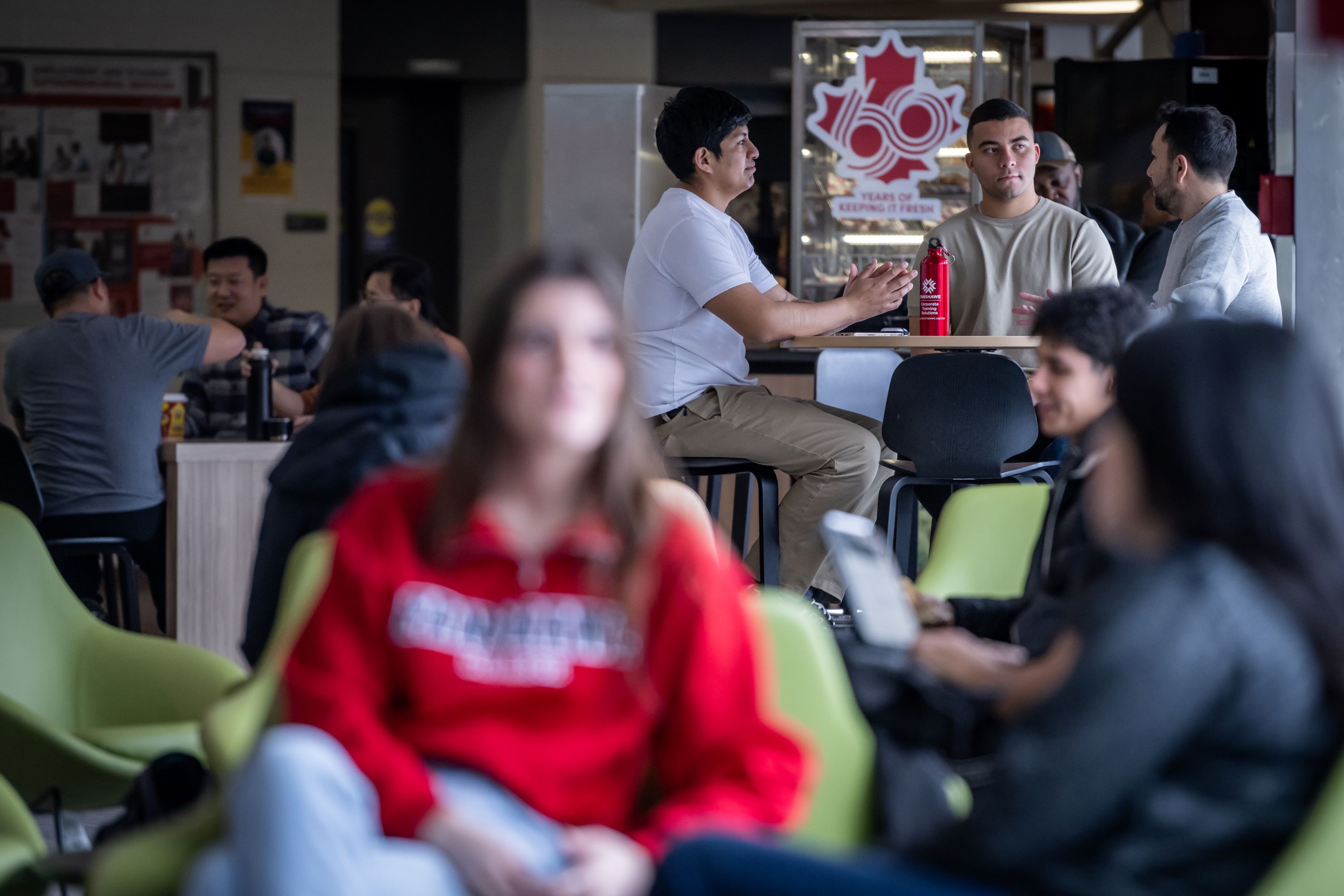Students sitting in chairs and at a table in a cafeteria.