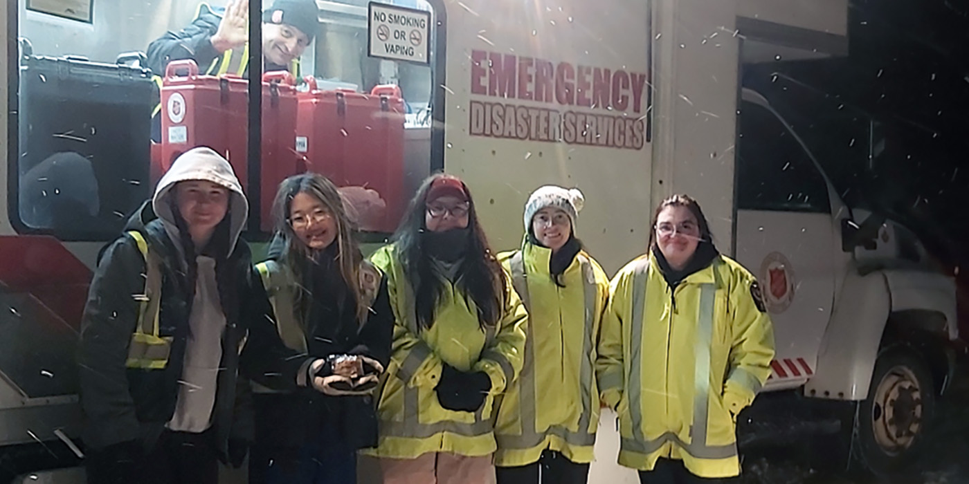 Five people in reflective coats in front of a white truck in the snow
