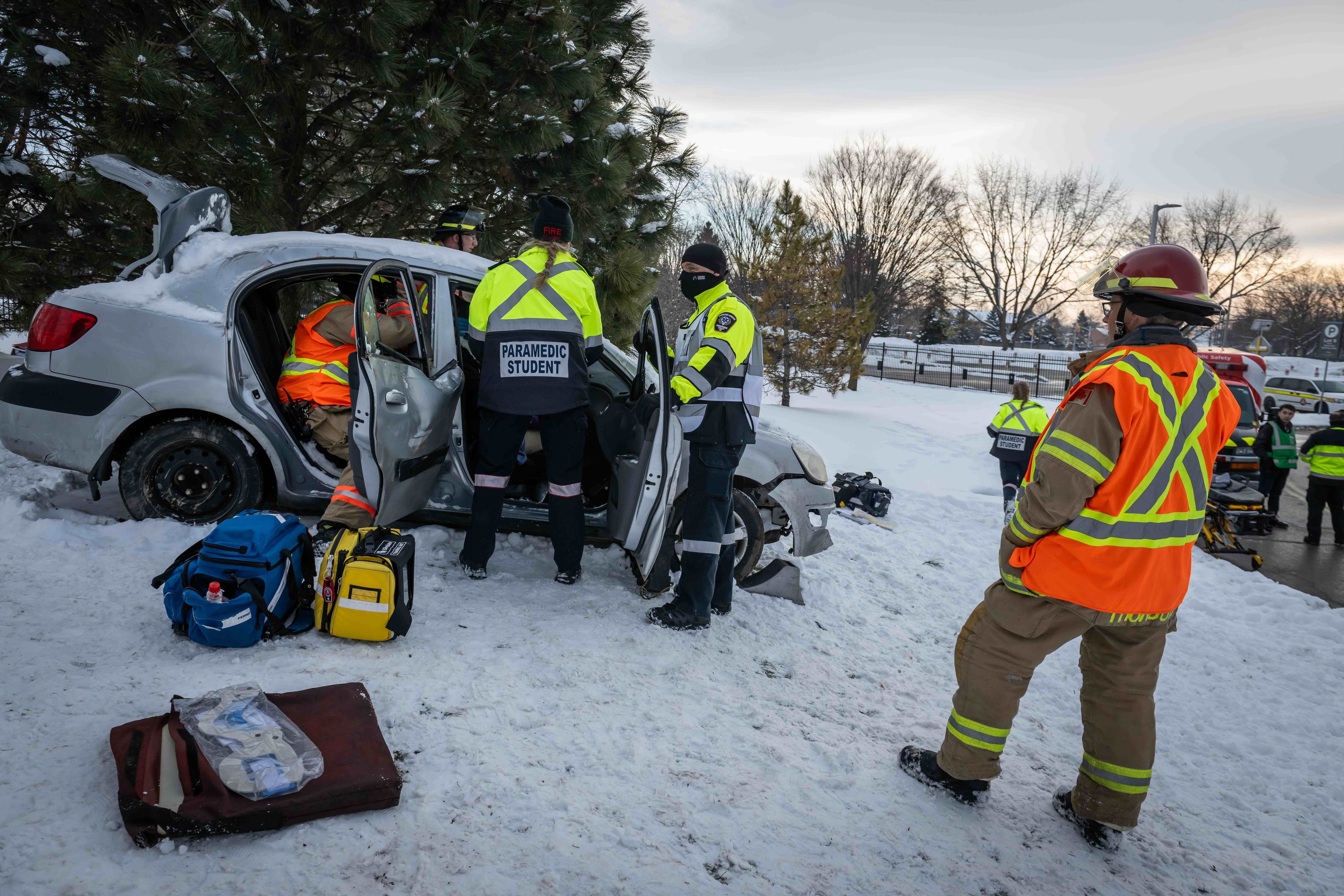 Paramedic students participate in a simulation at Fanshawe College's London Campus, responding to a car accident in snowy conditions, with emergency personnel and equipment visible.