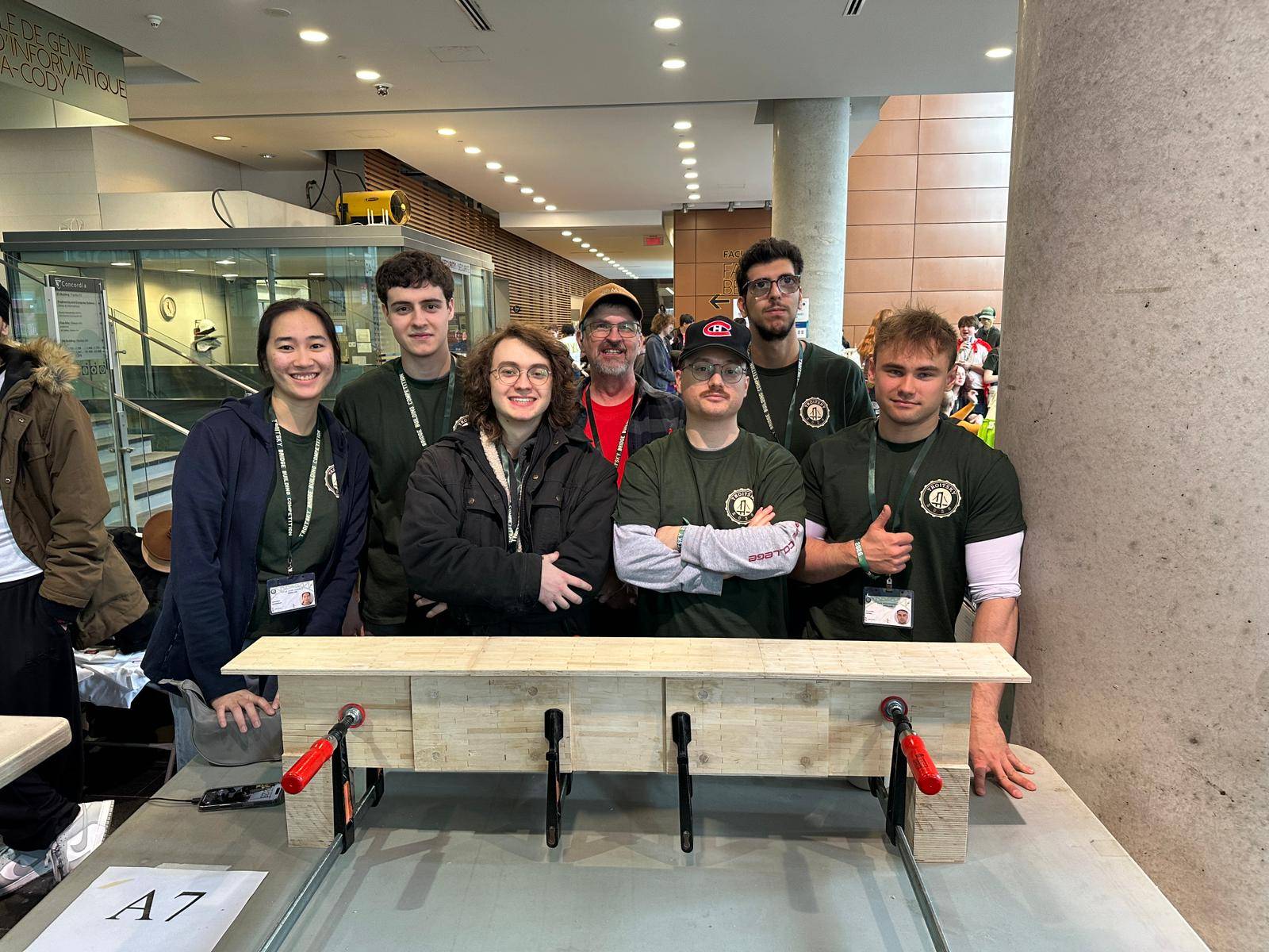 Seven students dressed in black stand behind a bridge they built using toothpicks, glue and dental floss.
