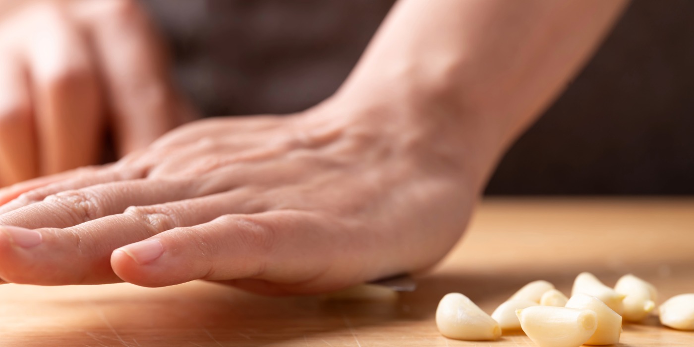 A palm placed on the flat size of a knife smashing garlic