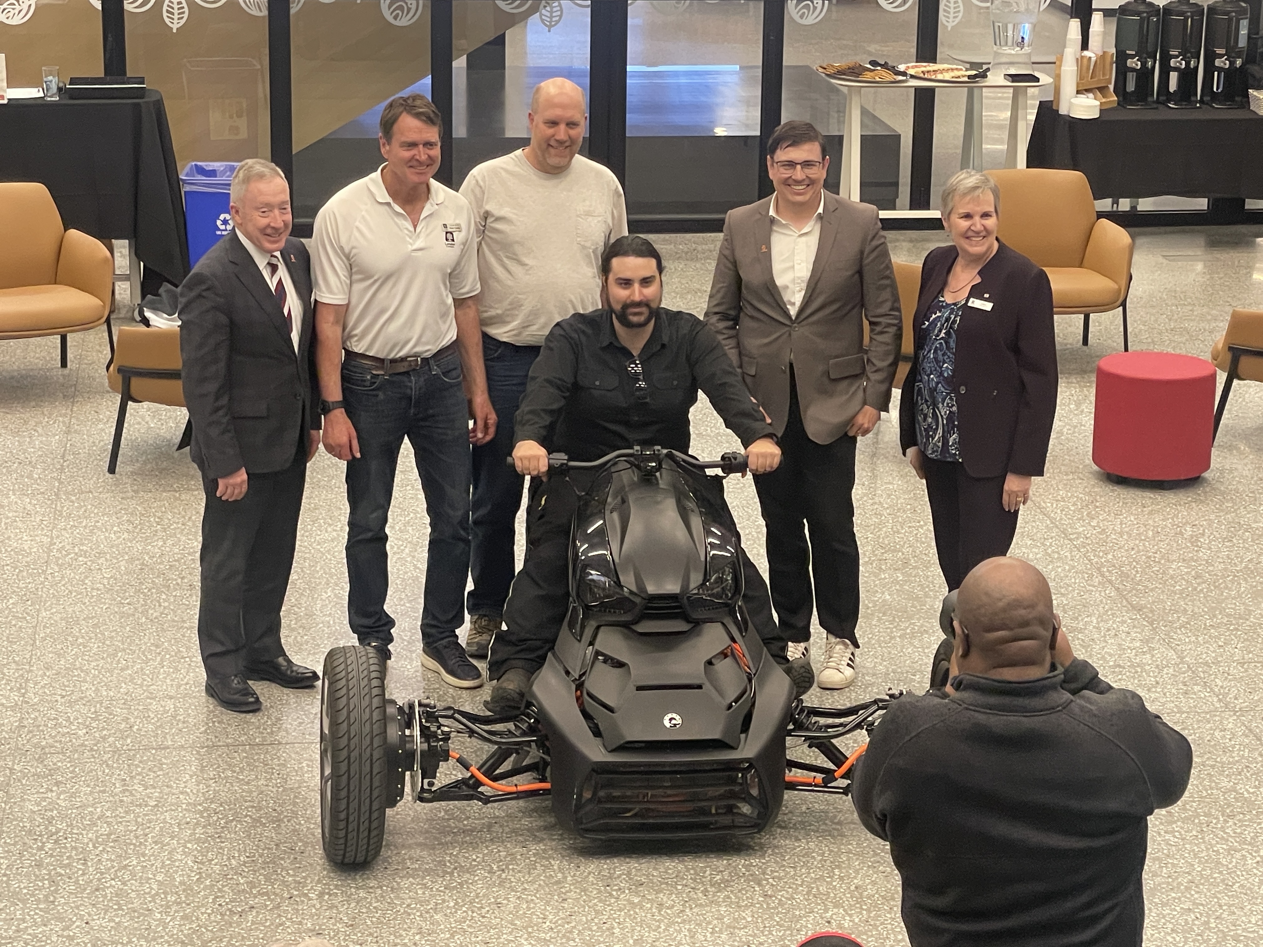 Six people work together to pull off a tarp to unveil a three-wheel black trike