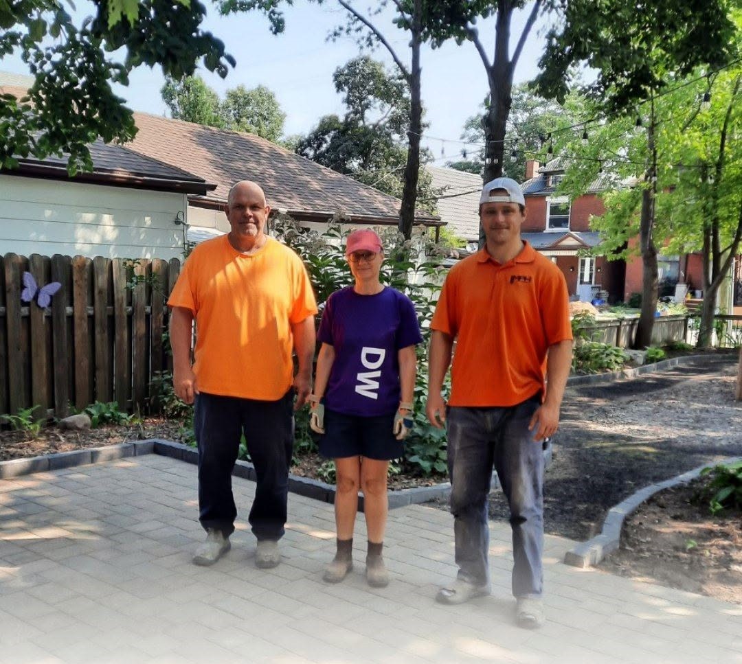 Two men and a women stand on a stone patio smiling. 