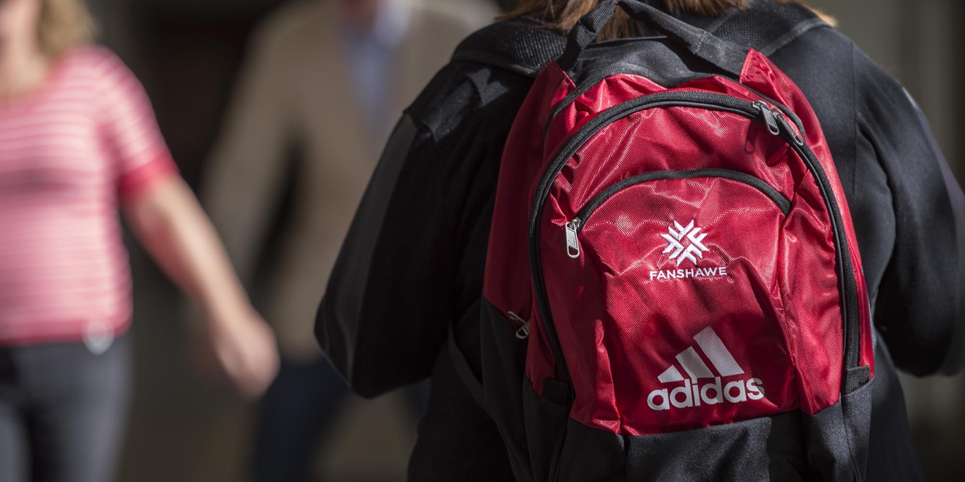 Student walking in hallway at Fanshawe College, wearing Fanshawe backpack