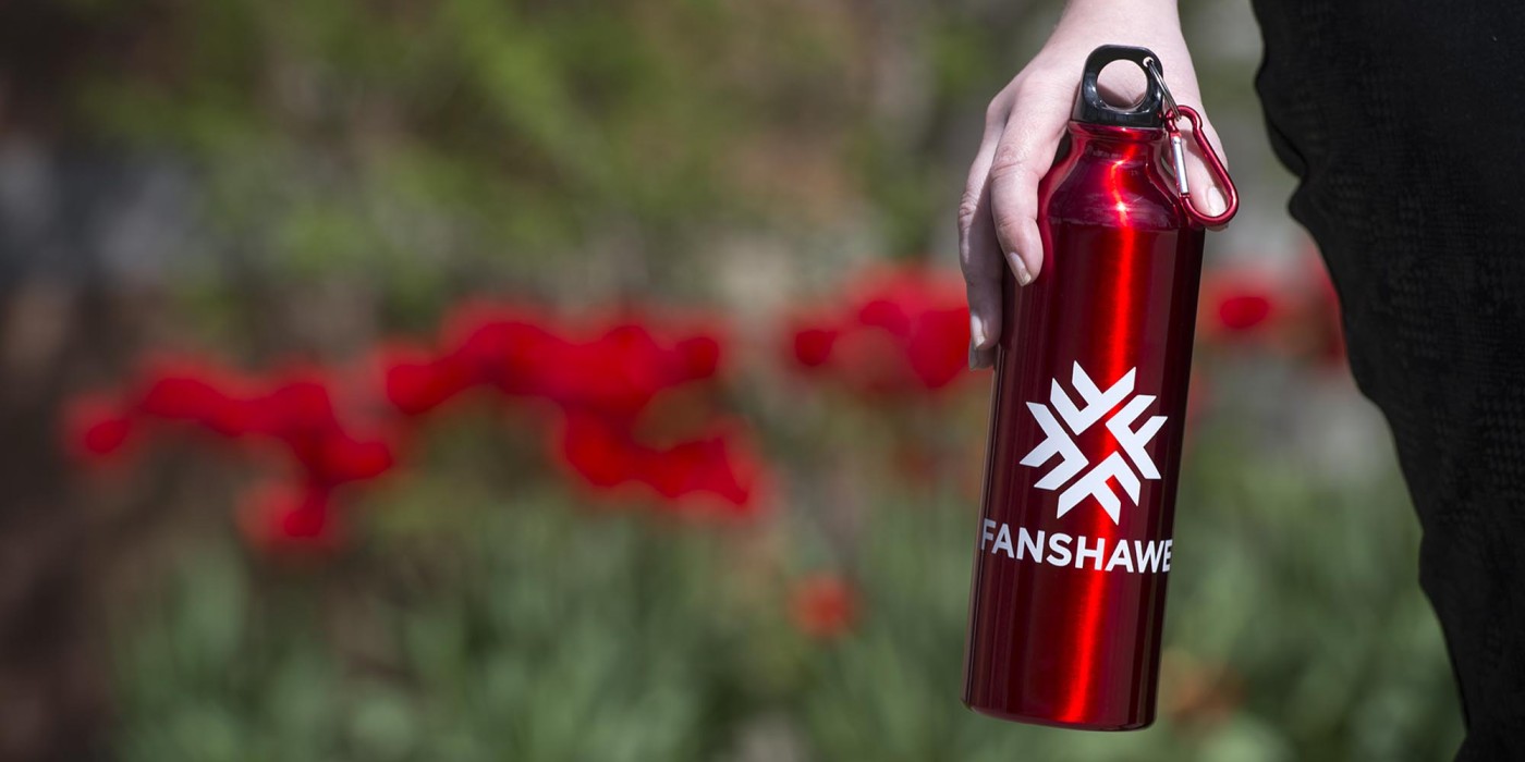 Student hand holding Fanshawe water bottle outdoors