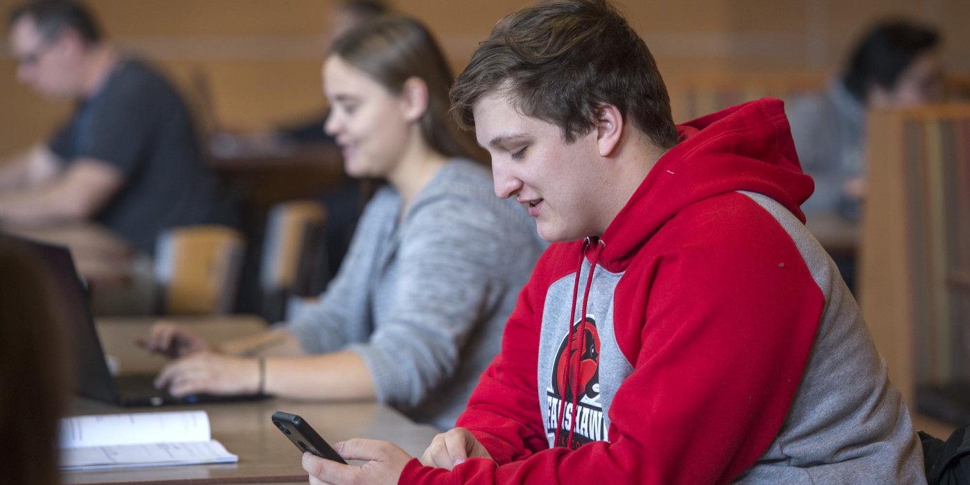 Fanshawe student sitting in cafeteria looking at mobile device