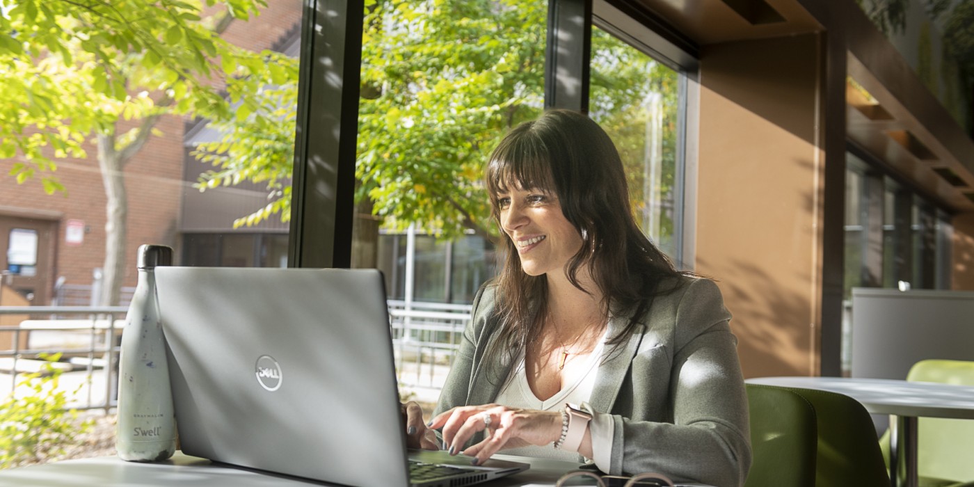 Photo of a student working on their laptop in a cafeteria
