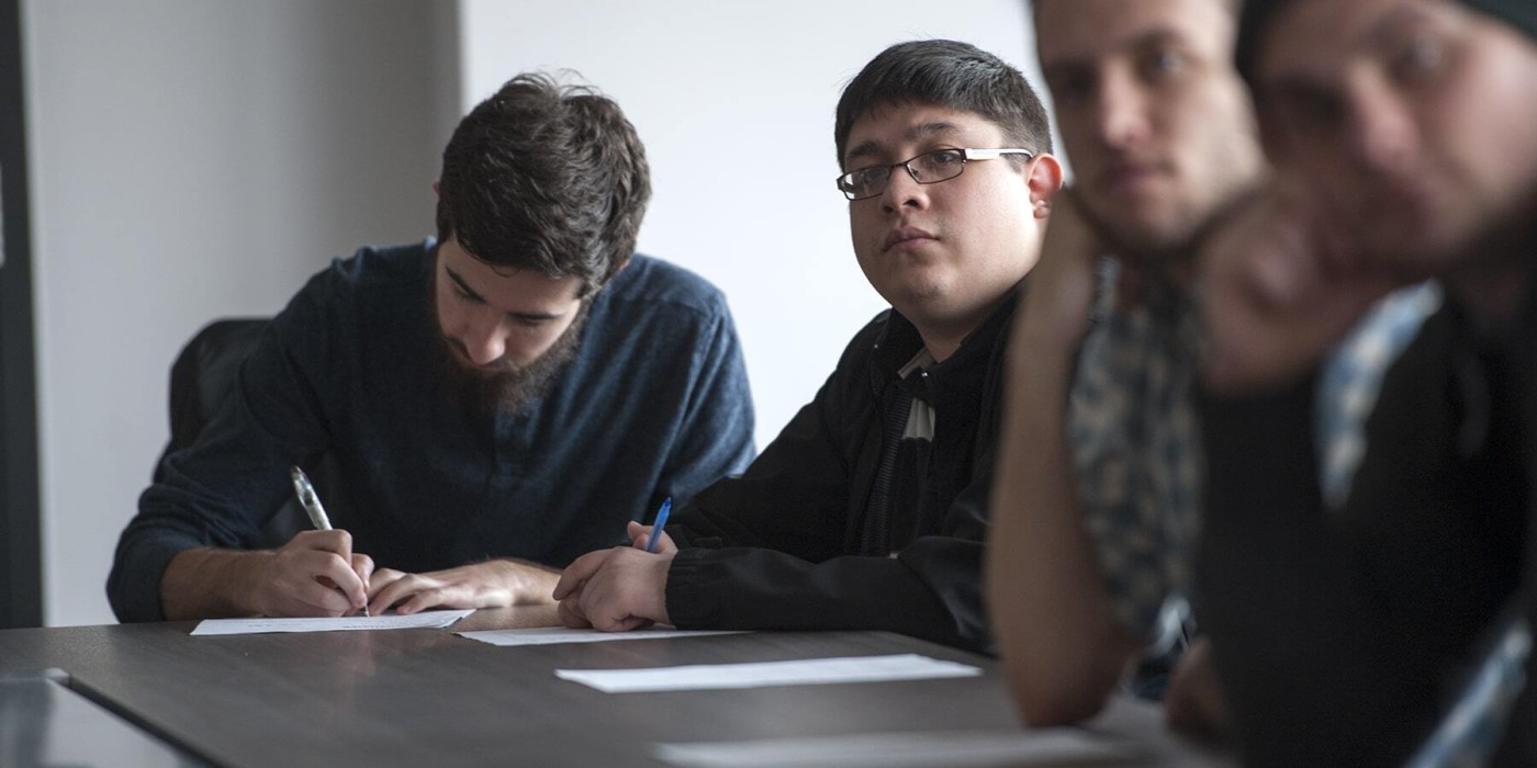 four men sitting at a table and one of them taking notes