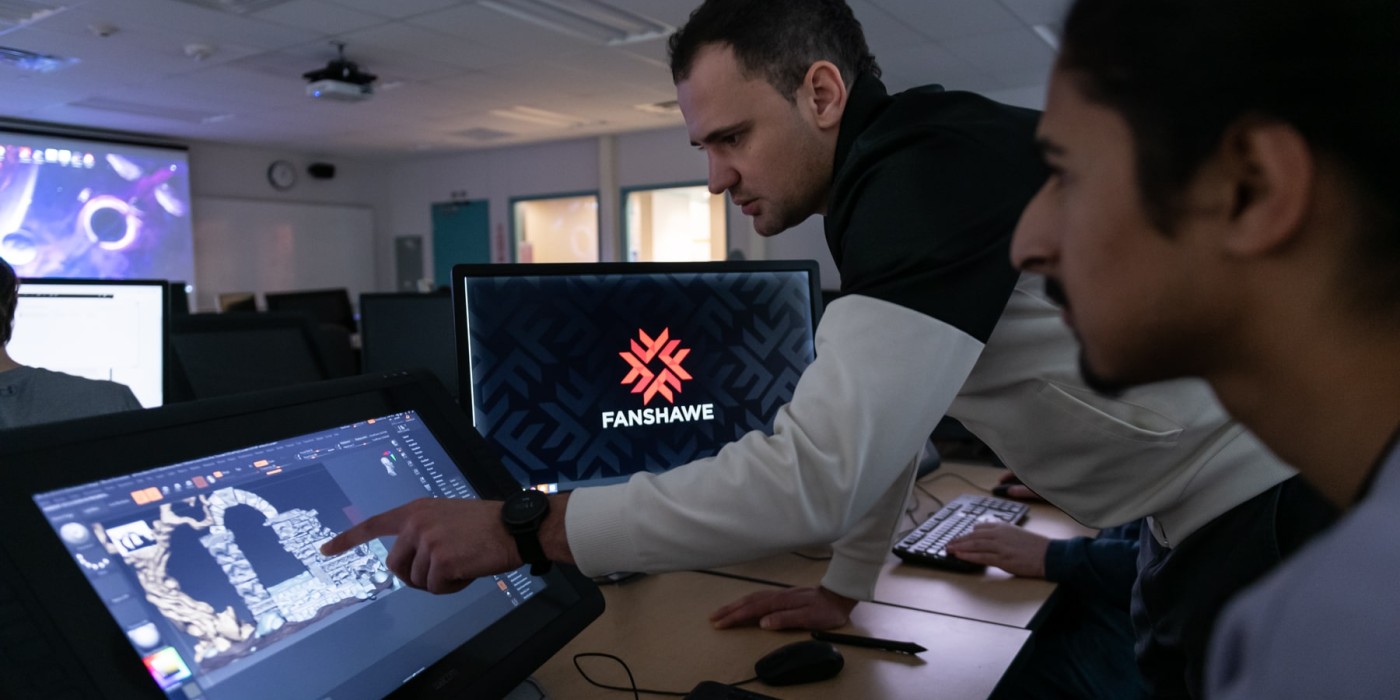 man points at video game concept on screen while student looks on