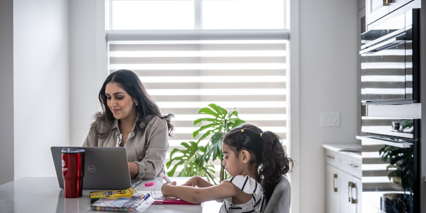 mother sits at laptop studying while daughter draws beside her