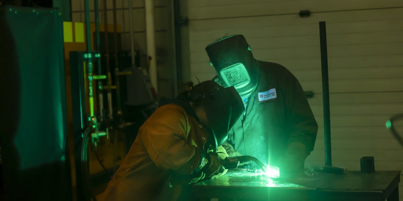 welders lean over their work lit by green welding light