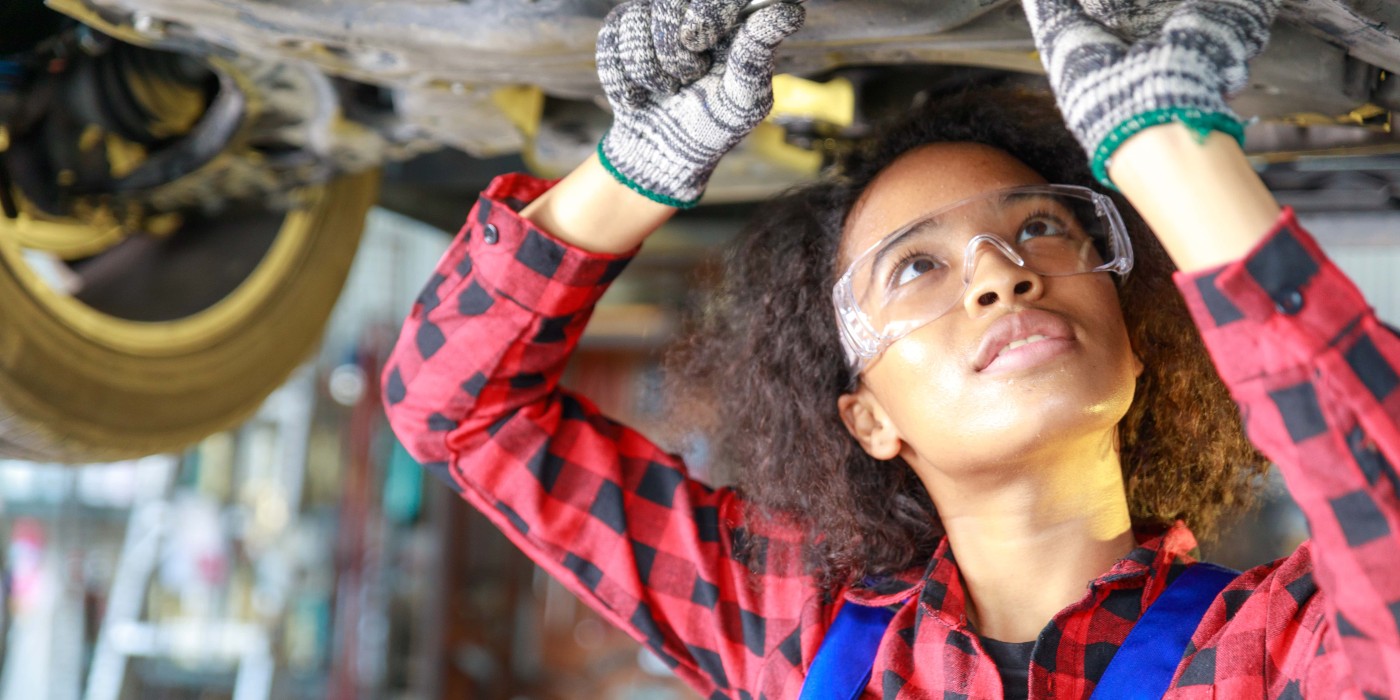woman wearing PPE works on underside of vehicle