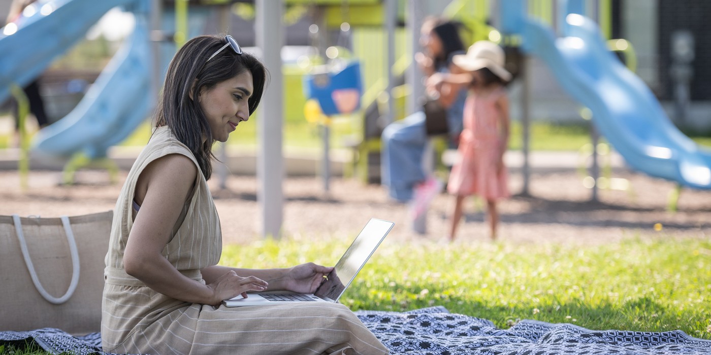 Mom studying on laptop at the park with her kids playing in the background