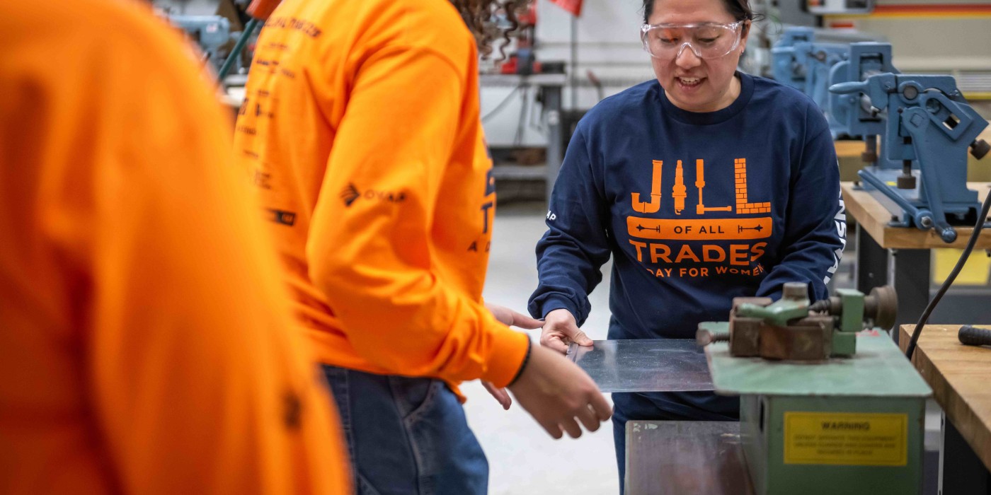 A female instructor guides a high school student through an activity during a Jill of All Trades event.