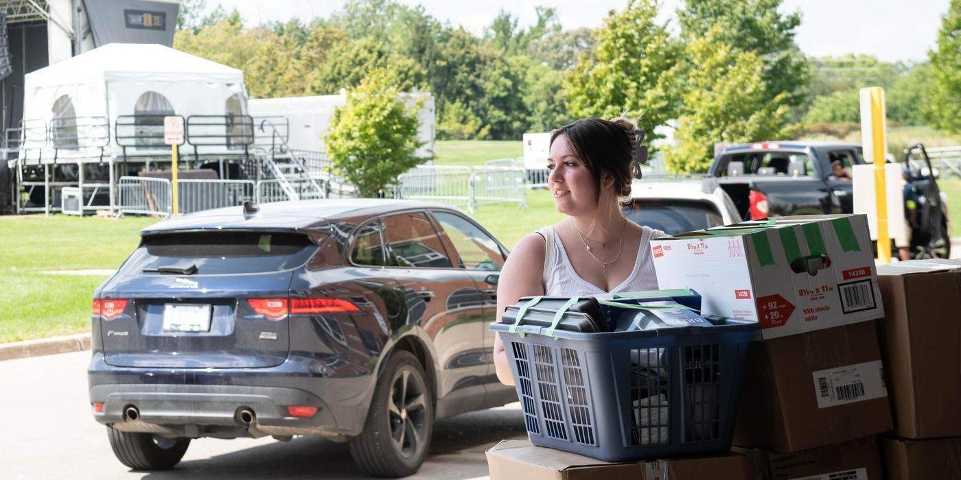 student stands by stack of packed boxes for moving