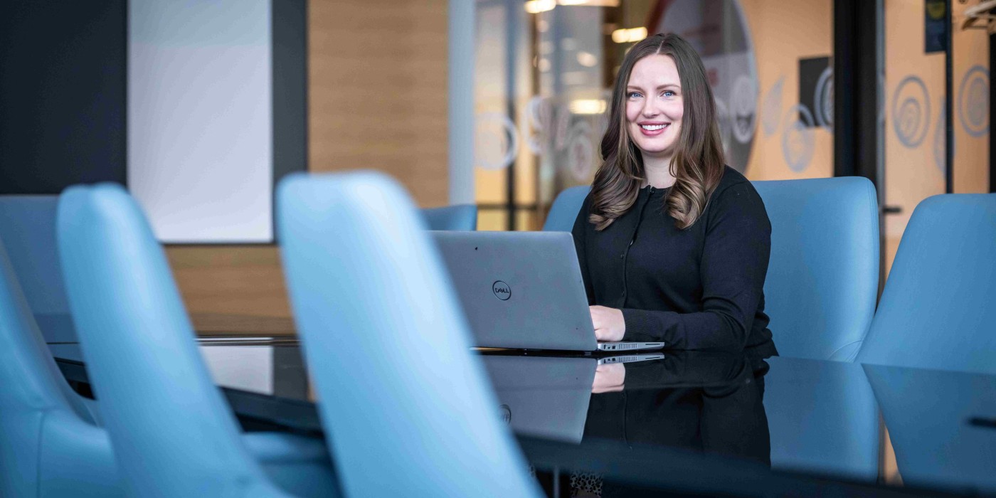 A Lawrence Kinlin student sitting in a board room on their laptop smiling at the camera