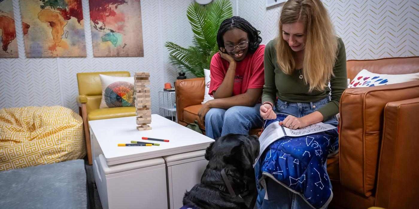 two students sit together in the Kind Space at Fanshawe, working with Heartley, the facility's dog for Canine Assistance Intervention