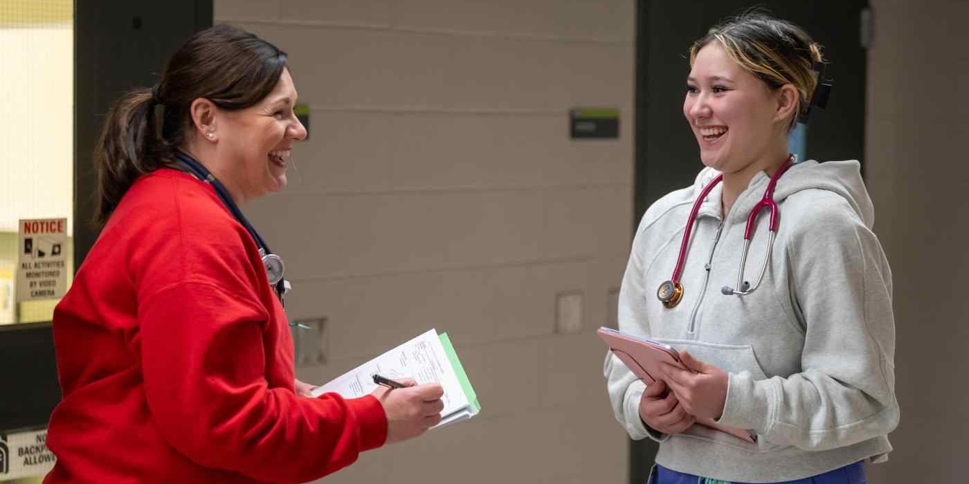 two nursing students with stethoscopes and clipboards laugh together