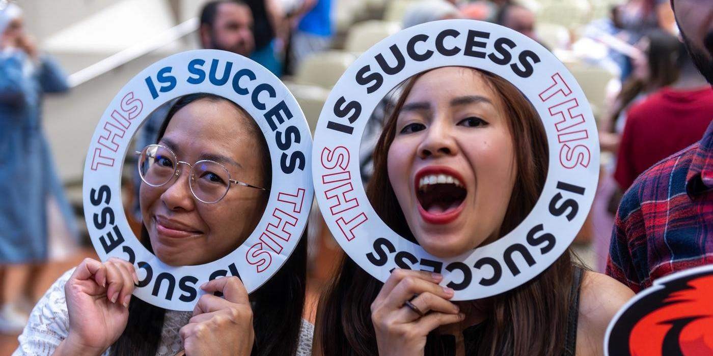 two students celebrate, holding this is success signs