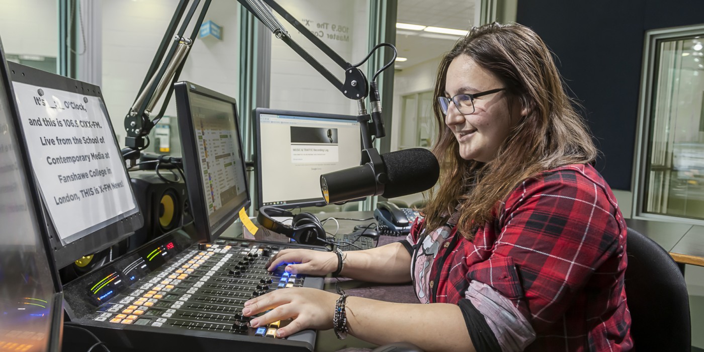 A student operates the audio board and speaks into a microphone in the 106.9 The X studio.