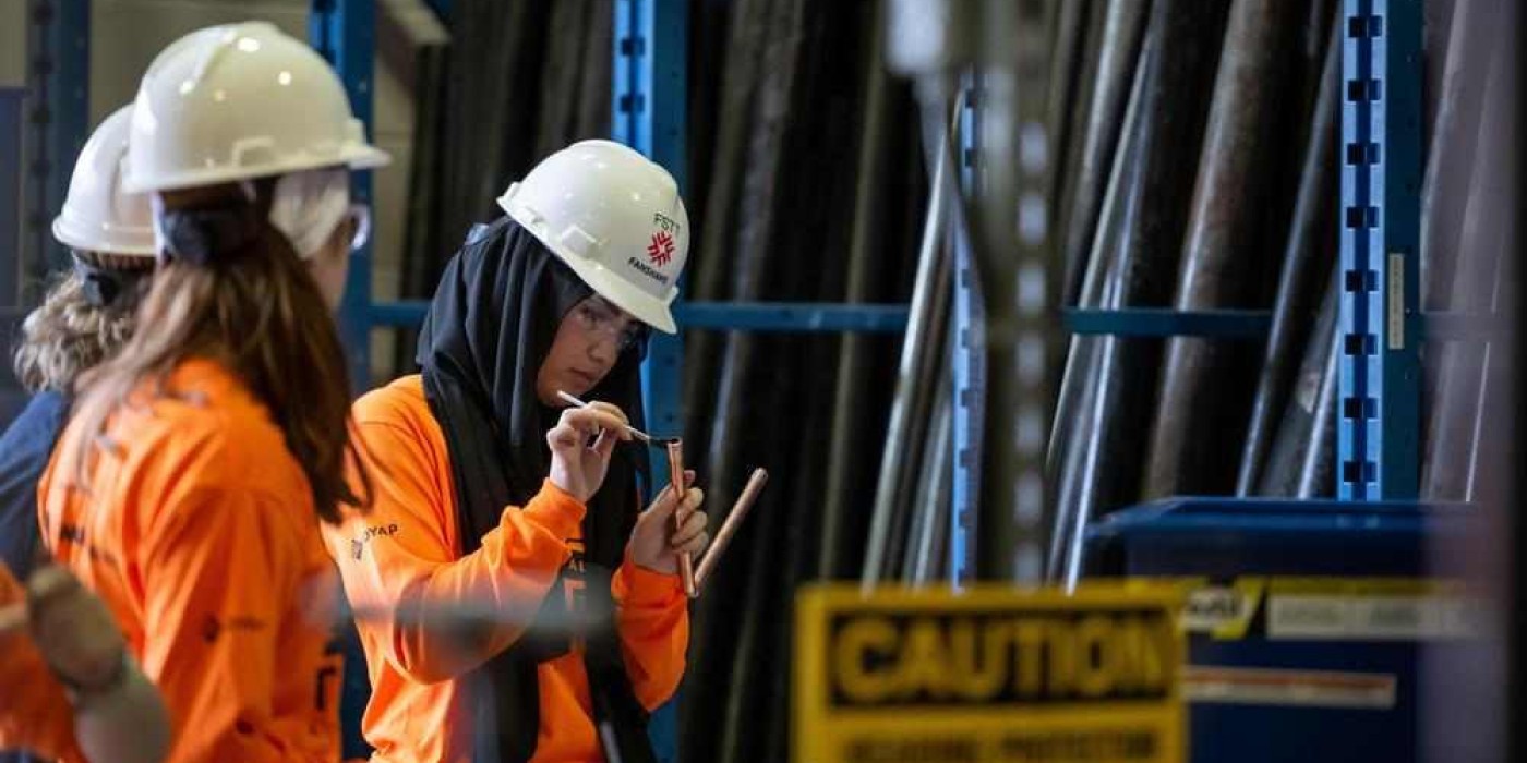 a person wearing a hard hat and safety glasses uses a small brush on a copper pipe