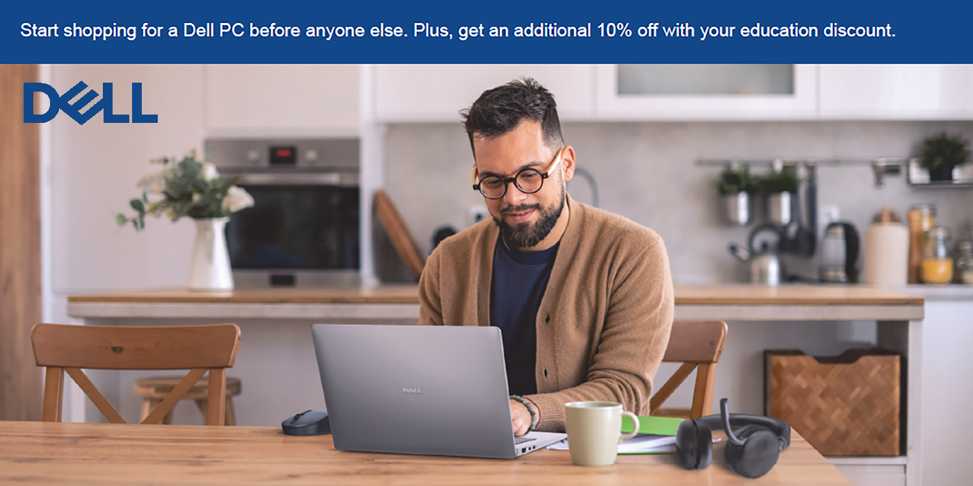 A man smiling and working on a laptop in a bright kitchen