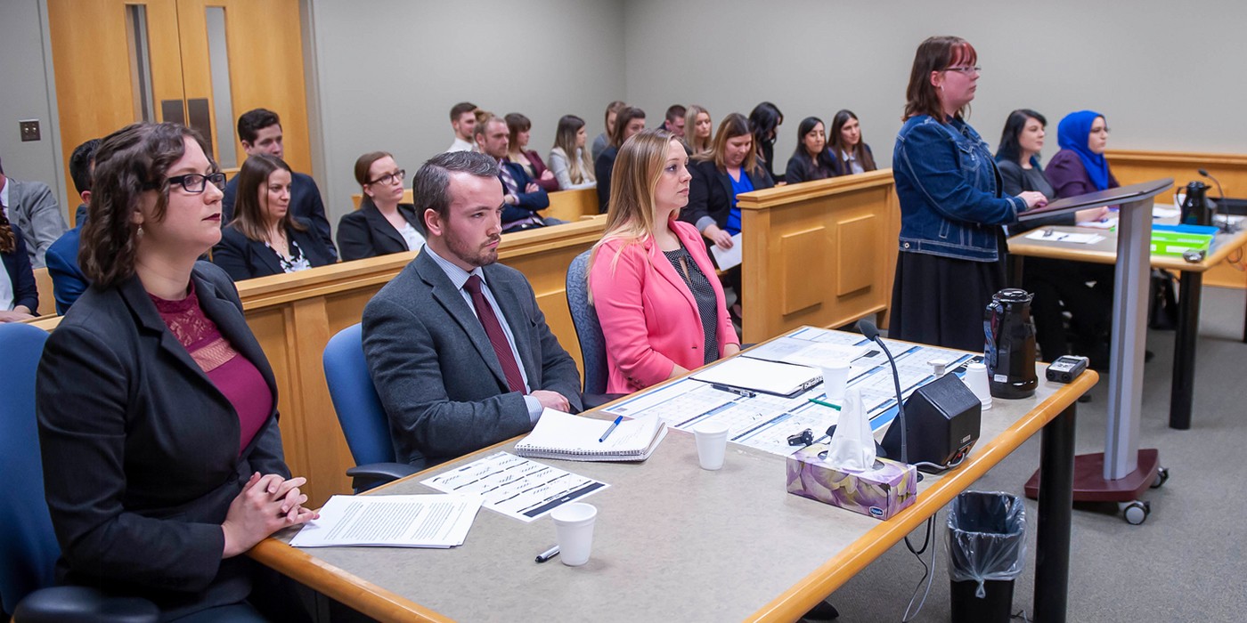 Students in formal attire sit in rows in a courtroom