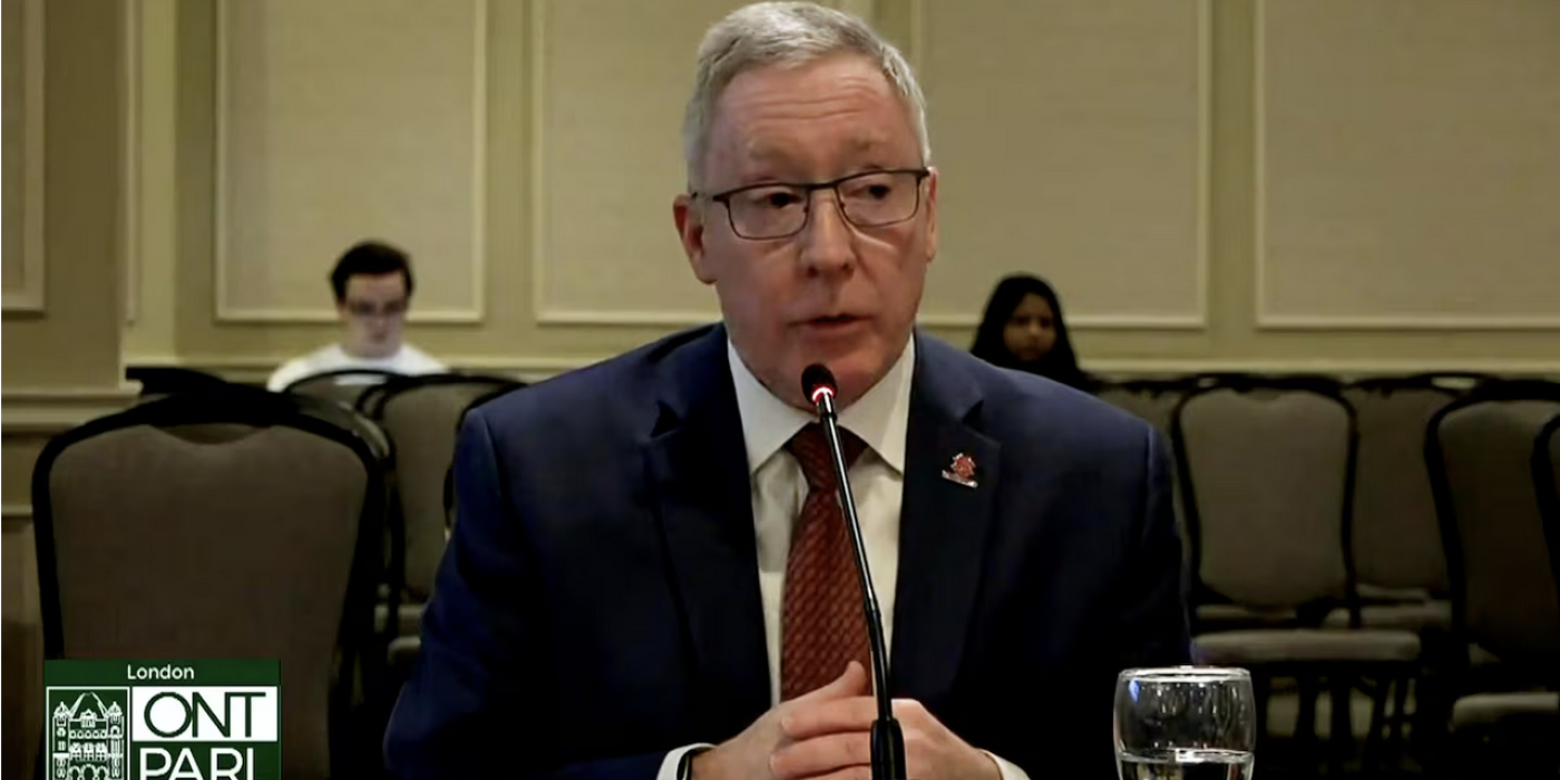 President Peter Devlin is seated at a table speaking into a microphone.
