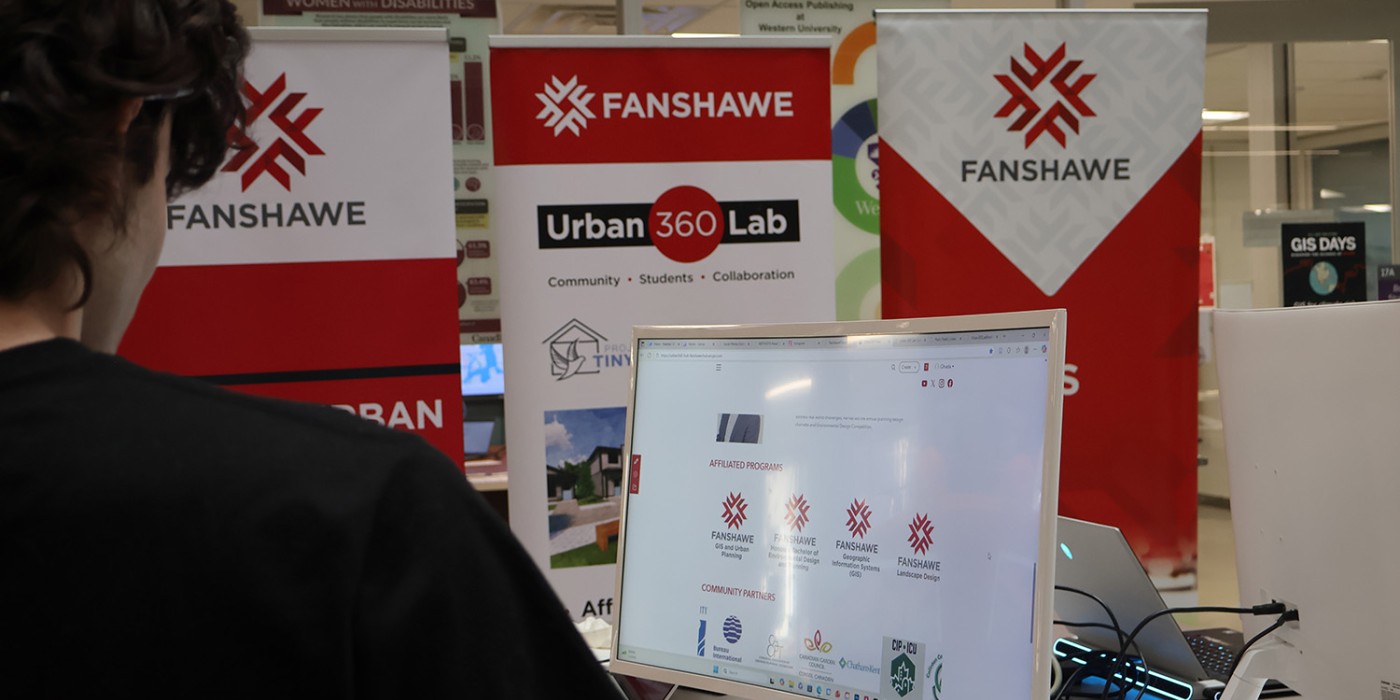 A person looks at a computer displaying a Fanshawe College webpage. Banners for Fanshawe and Urban 360 Lab are visible, suggesting an academic setting.