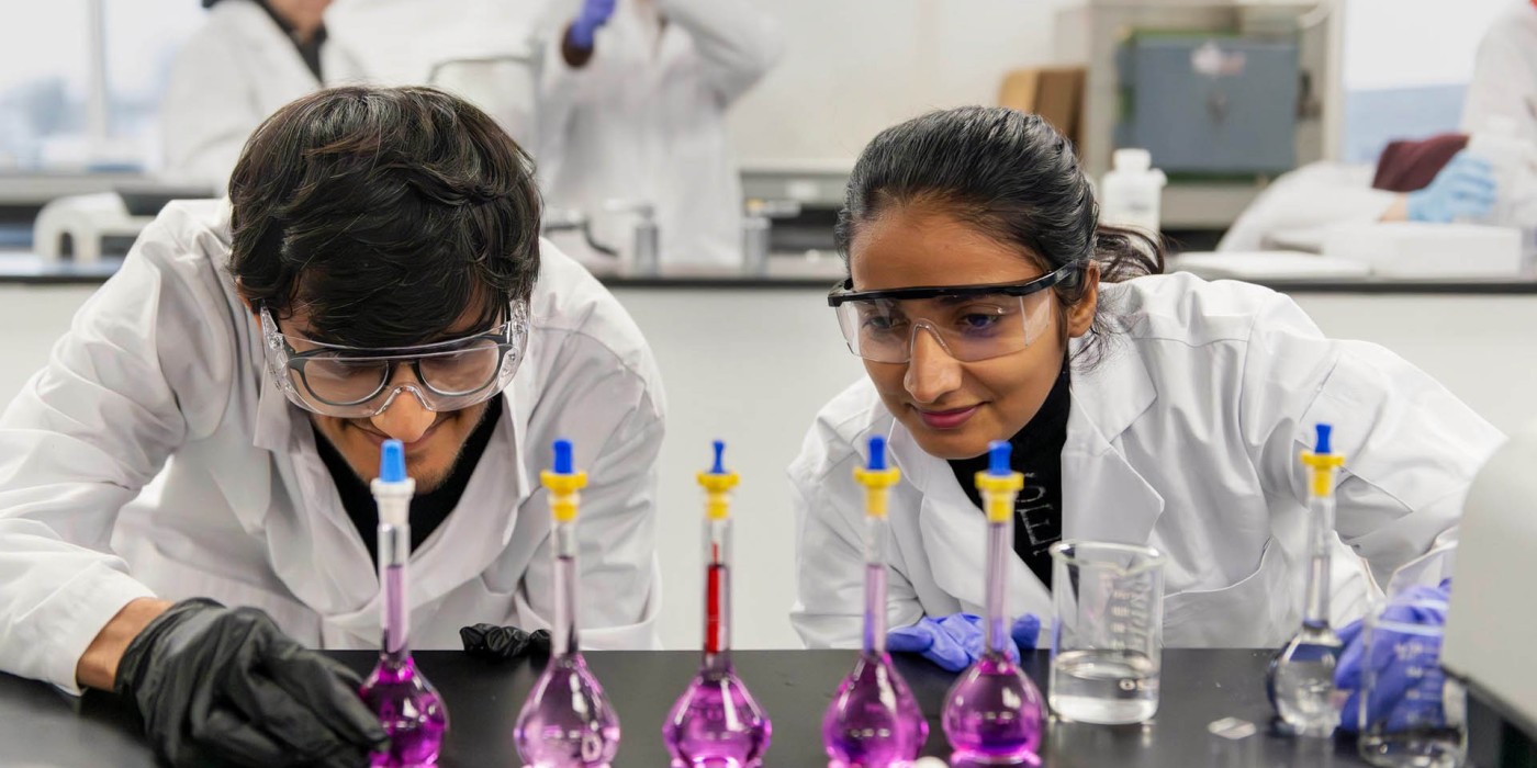 Two students in lab coats examine vials of liquid