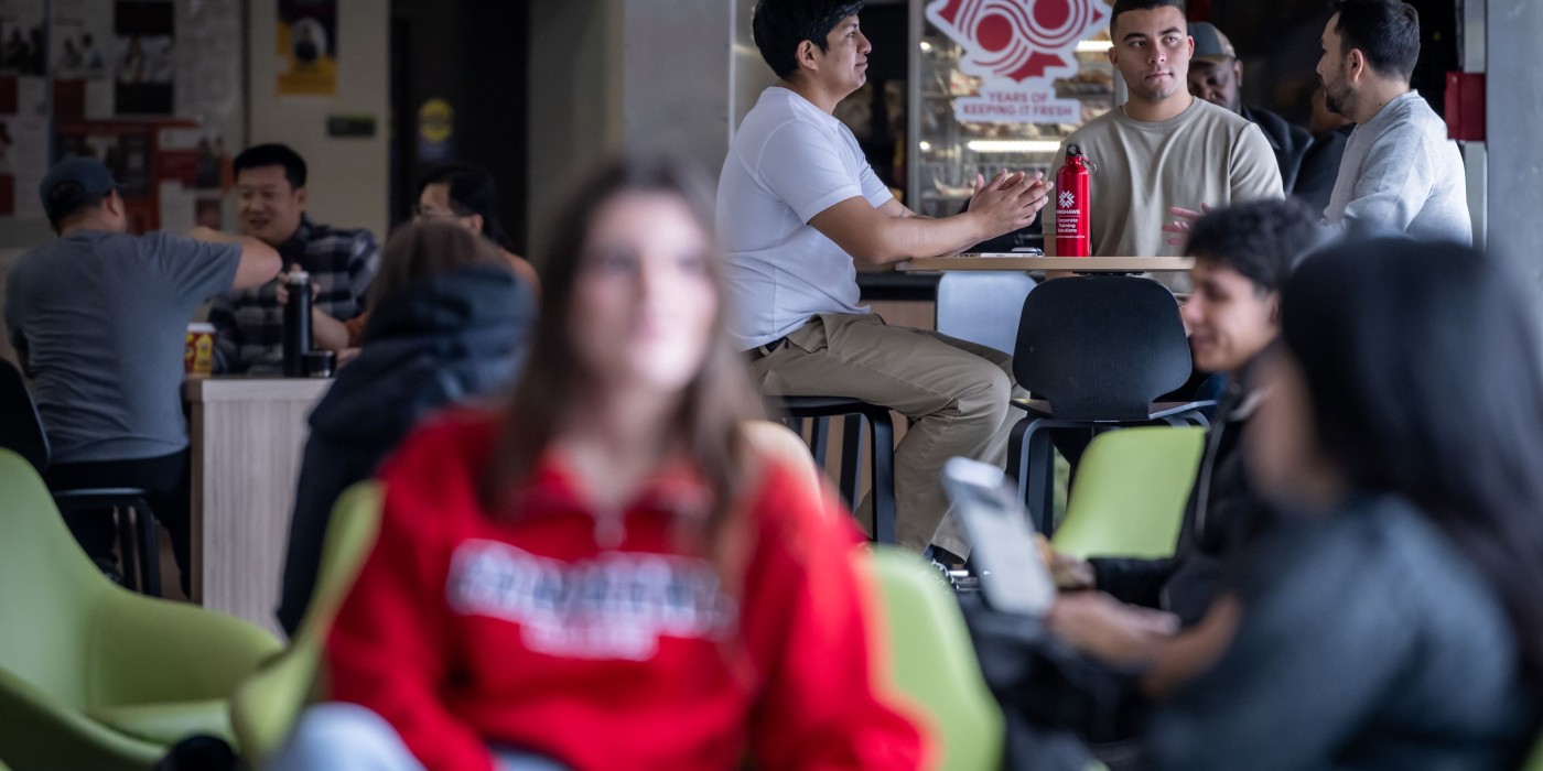 Students sitting in chairs and at a table in a cafeteria.