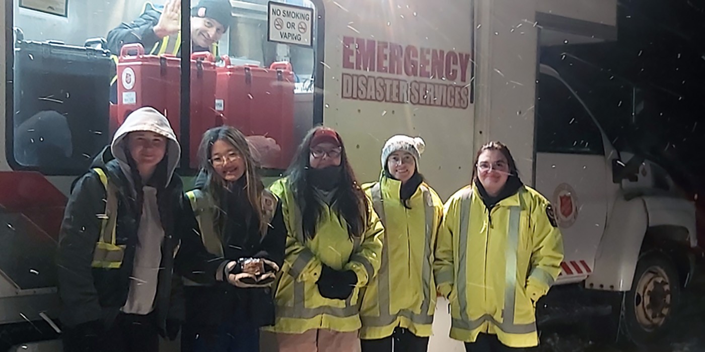 Five people in reflective coats in front of a white truck in the snow