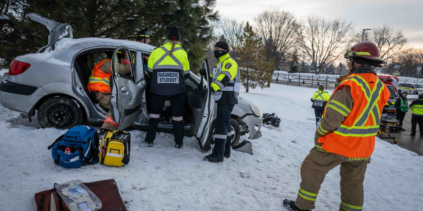 Paramedic students participate in a simulation at Fanshawe College's London Campus, responding to a car accident in snowy conditions, with emergency personnel and equipment visible.