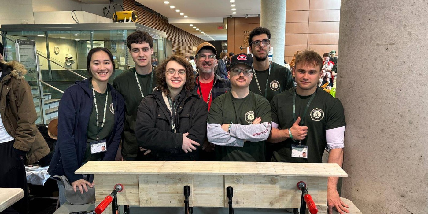 Seven students dressed in black stand behind a bridge they built using toothpicks, glue and dental floss.