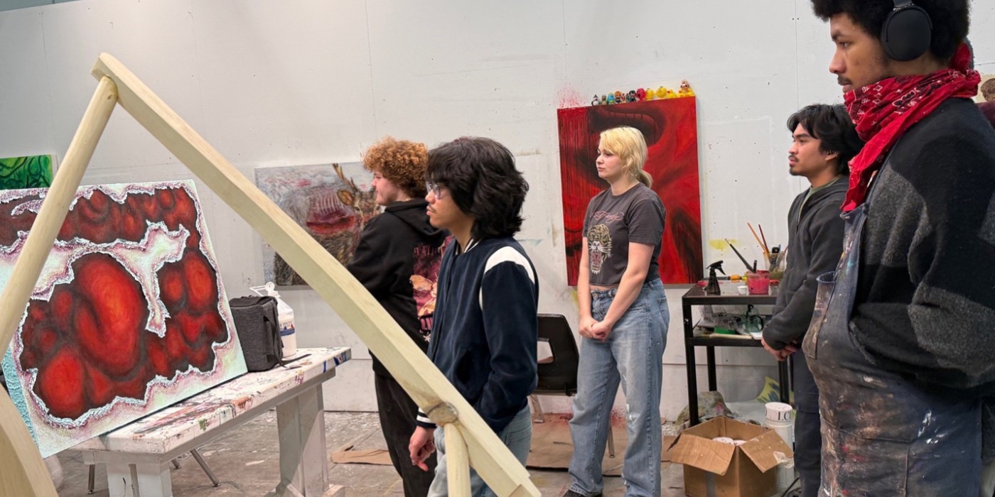 Students gather to examine a painted canvas with red and black shapes