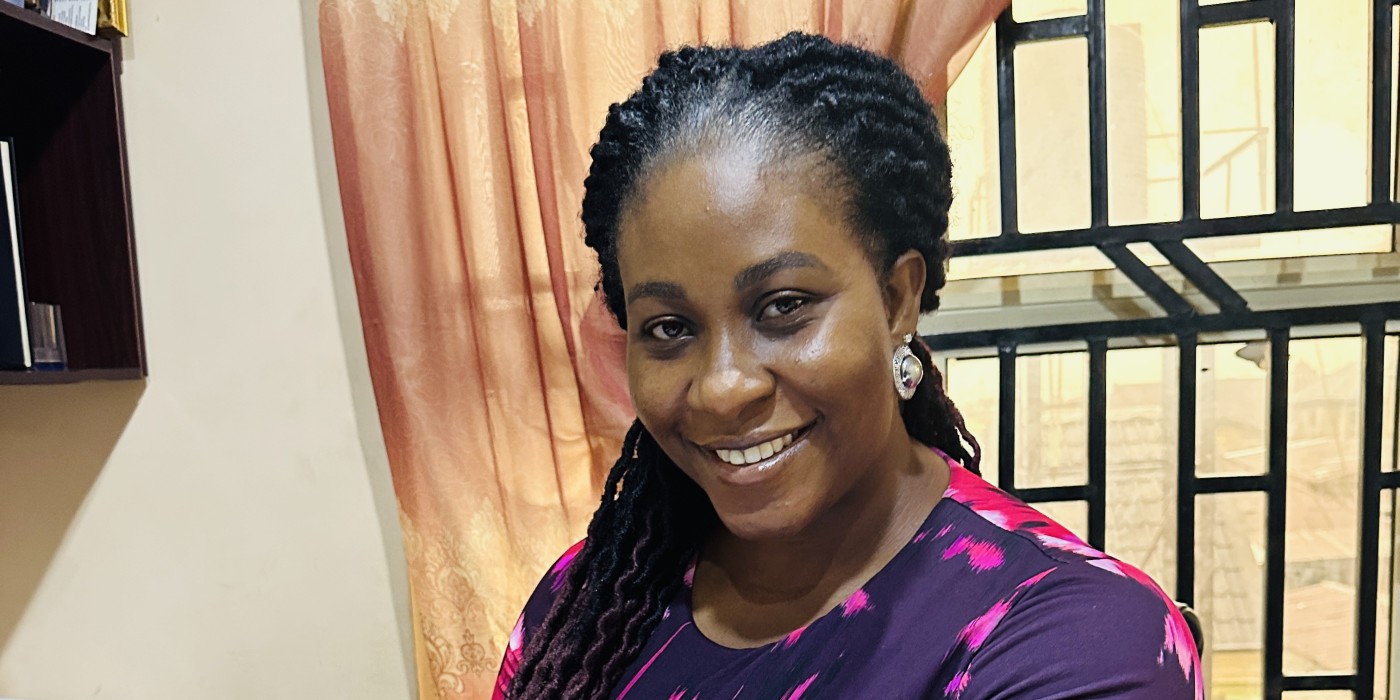 A woman in a pink and purple top smiles as she sits behind a desk full of papers.