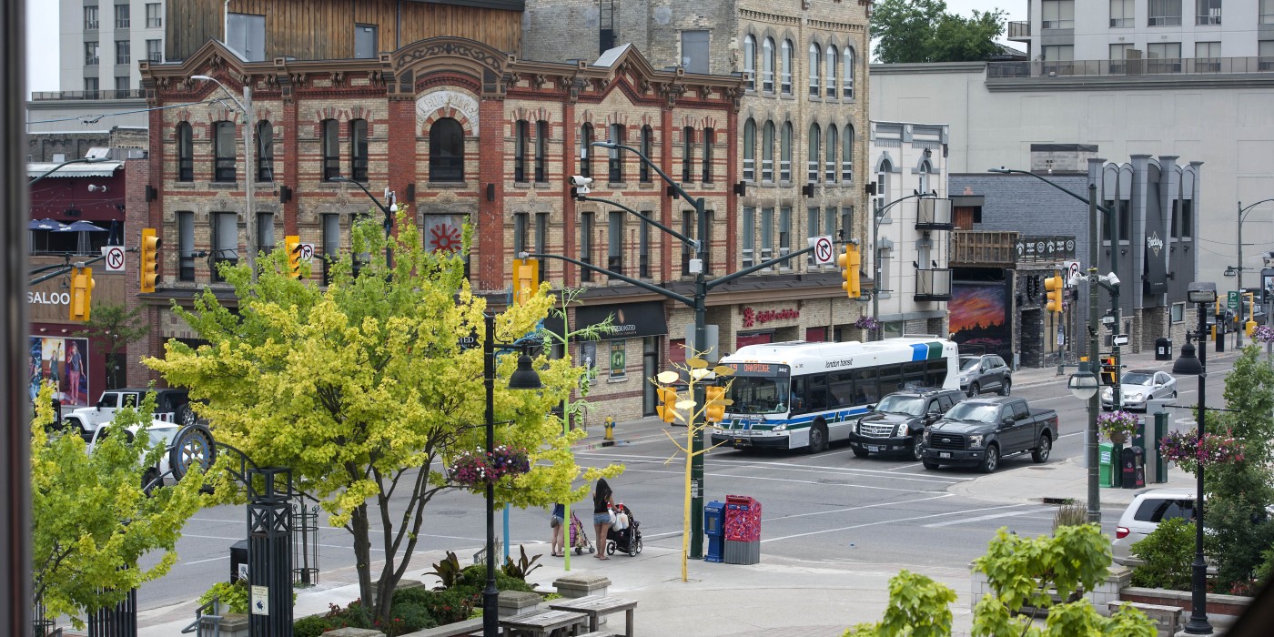 A view from a window overlooking a city street, where people are walking and vehicles are navigating the intersection, showcasing the urban environment and daily life.