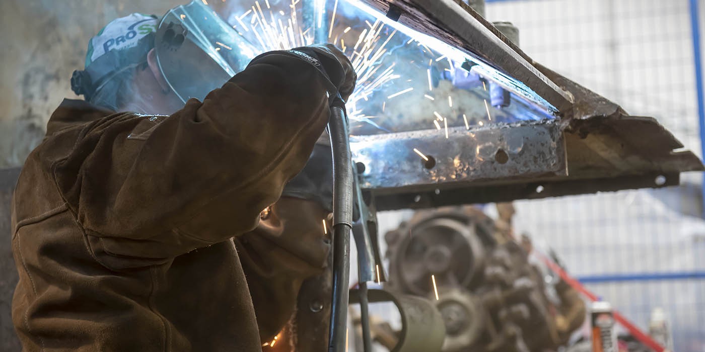 A person wearing protective gear welds metal, creating bright sparks.