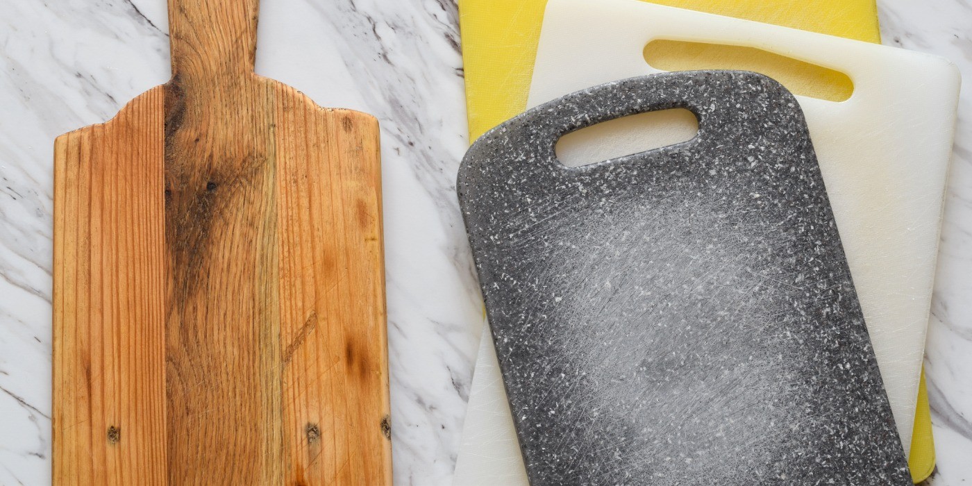 One wooden cutting board beside a stack of plastic cutting boards on a marble counter.