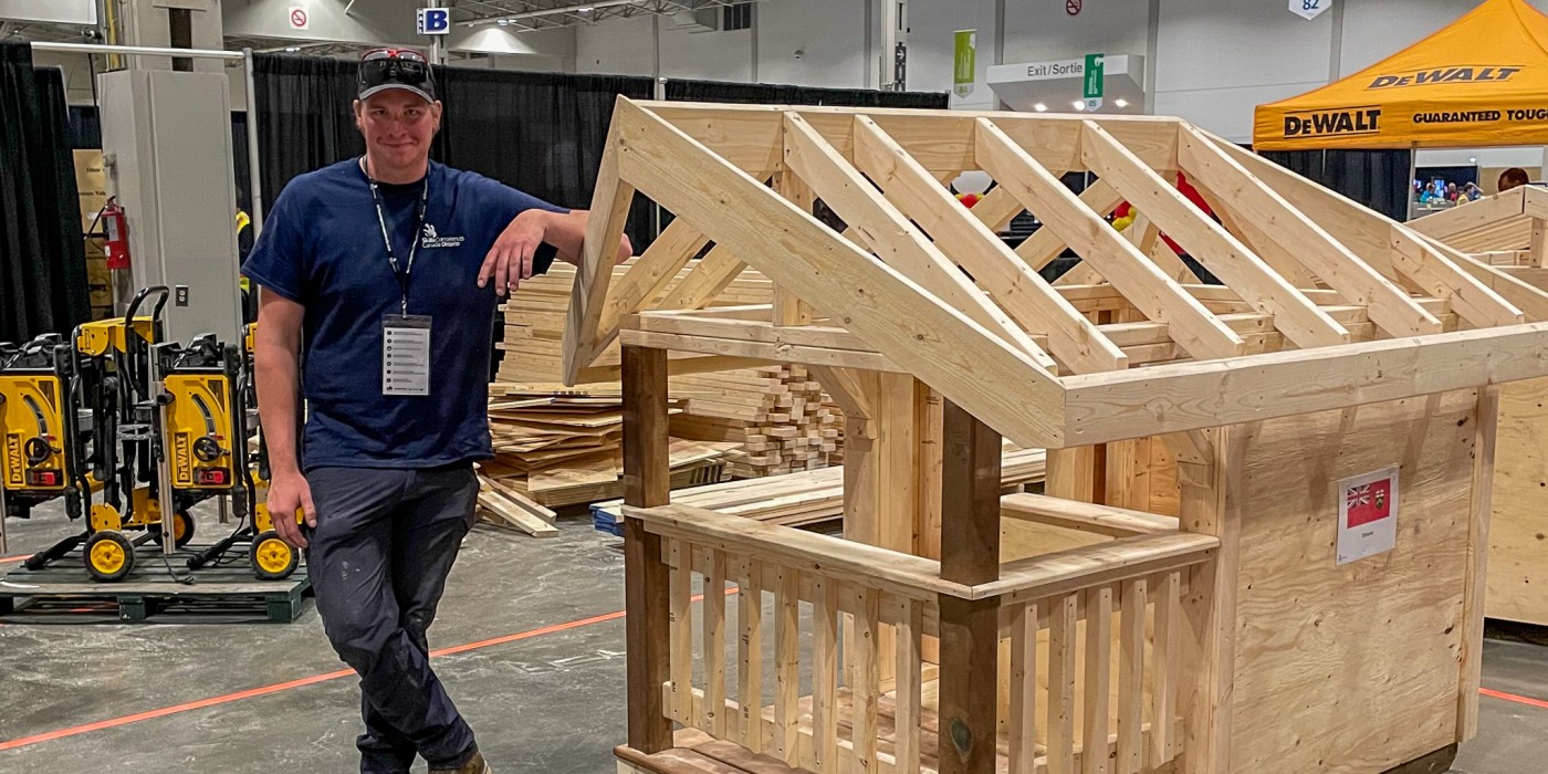 A carpentry apprentice stands next to a small structure he built during Skills Canada competition.